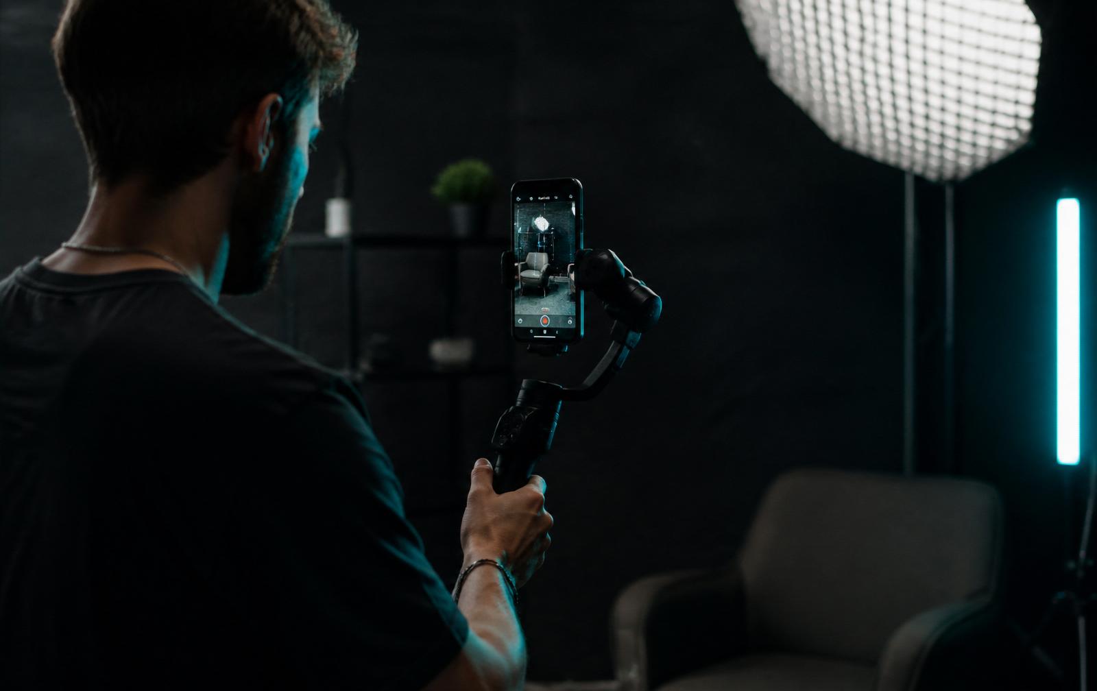 Tvůrce obsahu natáčí vertikální video na smartphone upevněný na gimbalu ve studiu s LED světlem